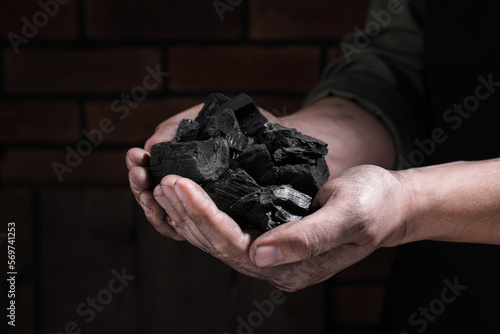 Man with handful of coal near brick wall, closeup view