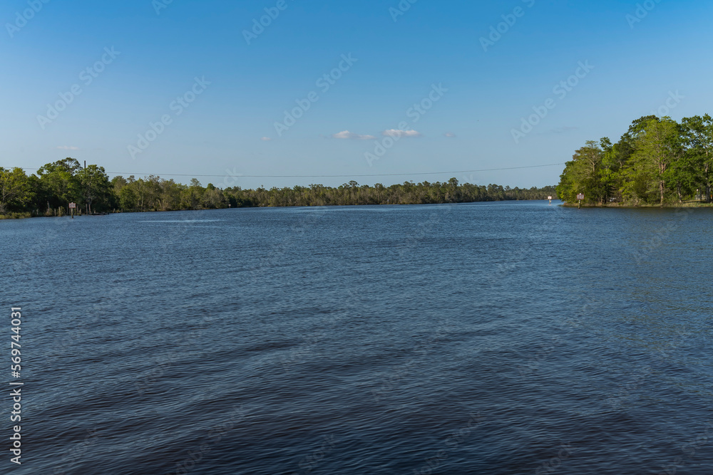 Wide river running through a forest in Milton, Florida. Large waterway of a river in between the green trees of a forests against the blue skyline background.