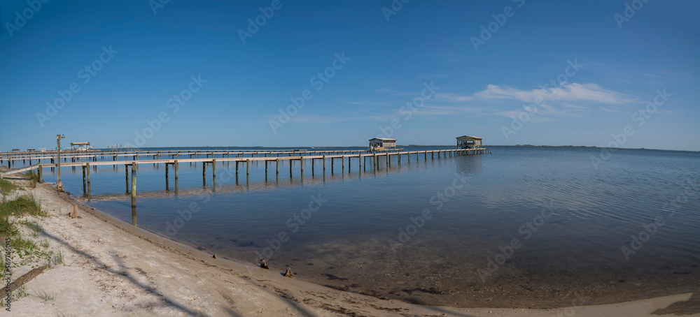Private docks with boat lifts against the blue sky background at Navarre, Florida. Views of dock from a shore with sand and grasses at the front.