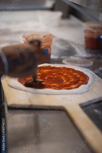 Close up of the making process, male hands applying tomato sauce on the dough. Preparing uncooked raw pizza plant-based with tomato sauce on a board.