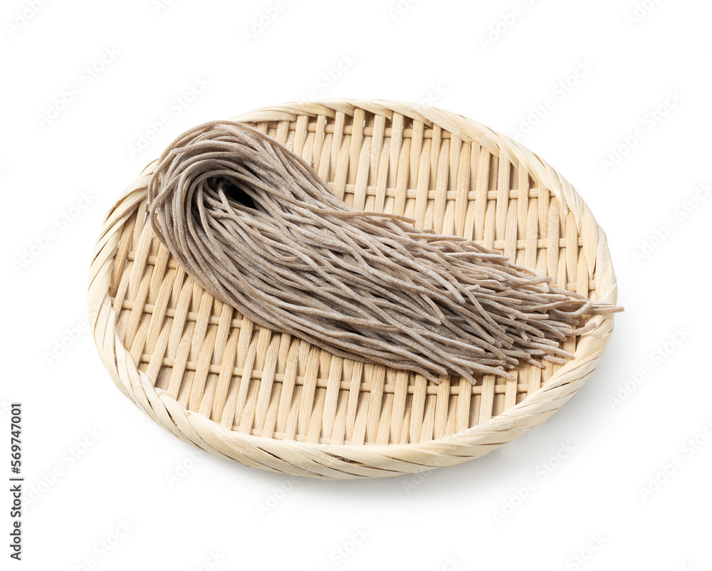 Raw soba noodles in a bamboo colander placed against a white background.