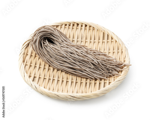 Raw soba noodles in a bamboo colander placed against a white background.