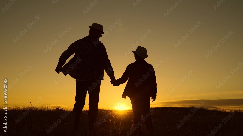 Dad plays with his kid outdoors in park. Father and son walk together holding hands in park at sunset. Silhouette, happy family, baby dad travel to sunset. Childhood dream, fatherly. Child adolescence