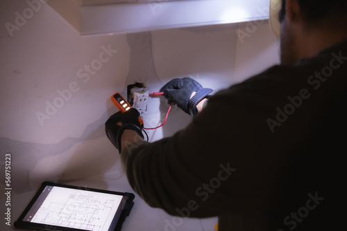 Electrician man wearing a helmet and gloves using a voltage tester to check the power in an electrical outlet