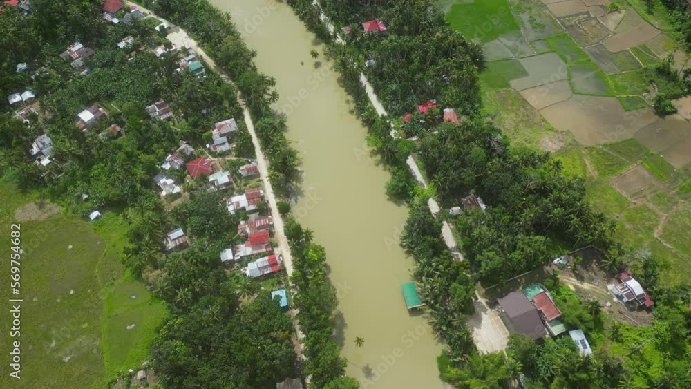 View from above of dirty village river with muddy water resembling swamp and surrounded by green trees and residential buildings. Dirty muddy water in river. Bad ecology that pollutes village river. View from above of dirty village river with muddy water resembling swamp and surrounded by green trees and residential buildings. Dirty muddy water in river. Bad ecology that pollutes village river.
