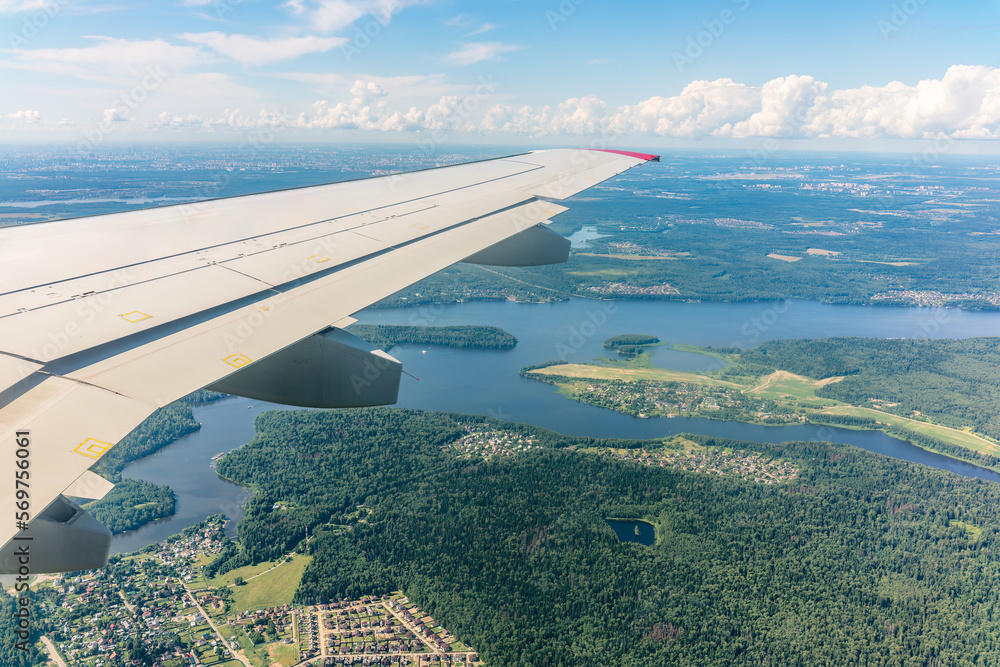 Obraz premium View of airplane wing, blue skies and green land during landing. Airplane window view.