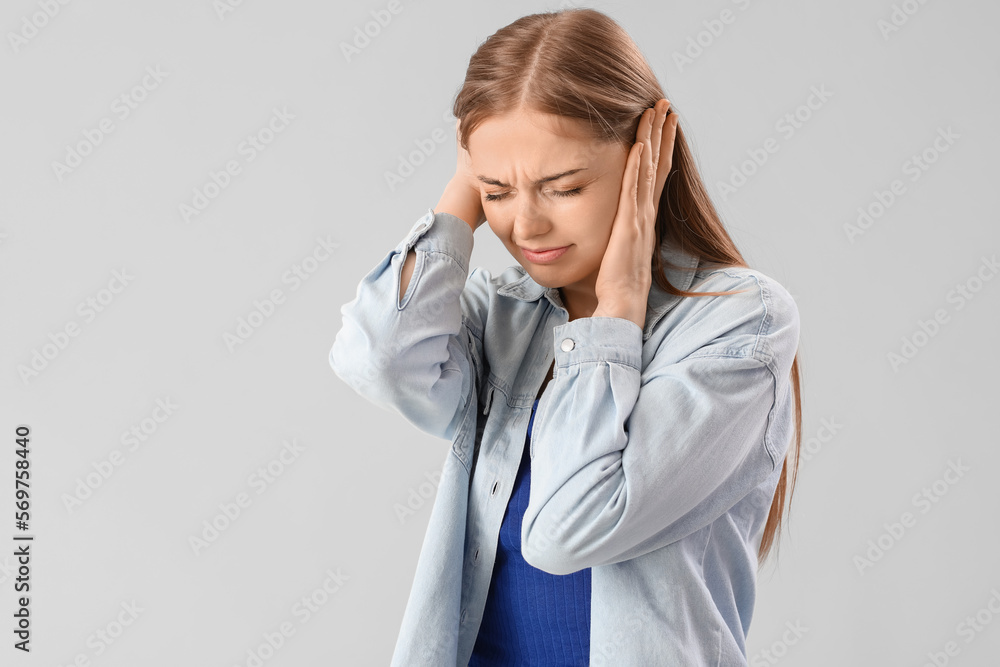 Young woman suffering from loud noise on grey background Young woman suffering from loud noise on grey background