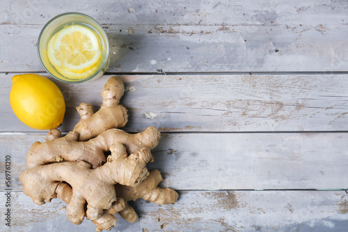 Fresh ginger roots, glass of water and lemon on wooden background