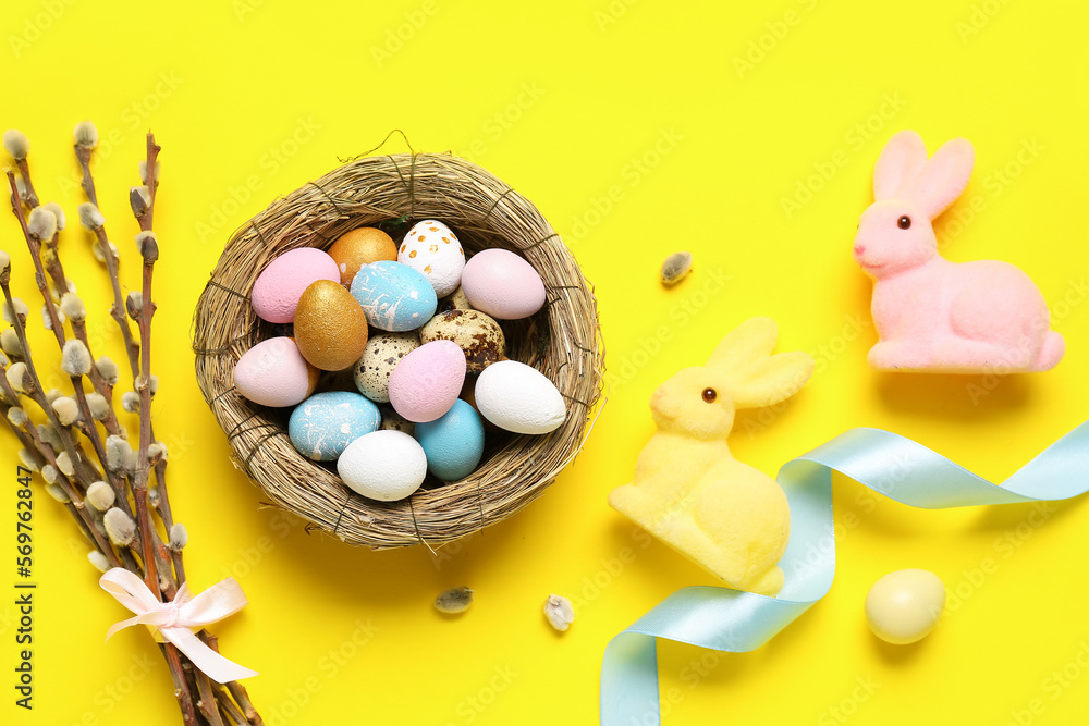 Composition with nest of Easter eggs, willow branches and toy bunnies on yellow background Stock