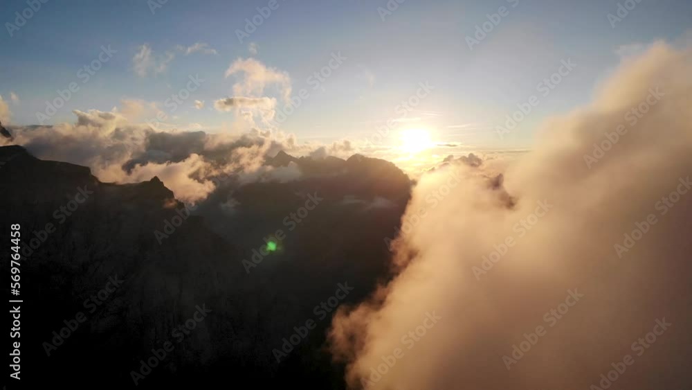 Flight between glowing clouds during a sunset in the Swiss Alps as the sun disappears behind clouds and mountain peaks