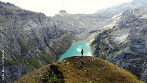 A standing hiker enjoying the view over lake Limmernsee in Glarus, Switzerland, the turquoise colored water of which is surrounded by tall Swiss Alps peaks and cliffs photo