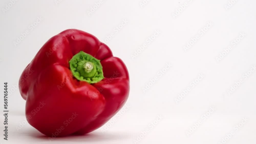 Whole, bright red bell pepper vegetables falling onto white table top and bouncing into each other before settling close up in slow motion Whole, bright red bell pepper vegetables falling onto white table top and bouncing into each other before settling close up in slow motion