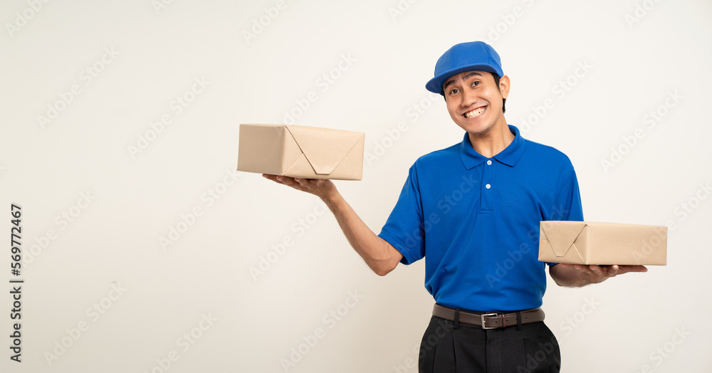 Happy delivery asian man in blue uniform standing holding box parcel cardboard on isolated white background. Smiling male service worker. Delivery courier and shipping service. Happy delivery asian man in blue uniform standing holding box parcel cardboard on isolated white background. Smiling male service worker. Delivery courier and shipping service.