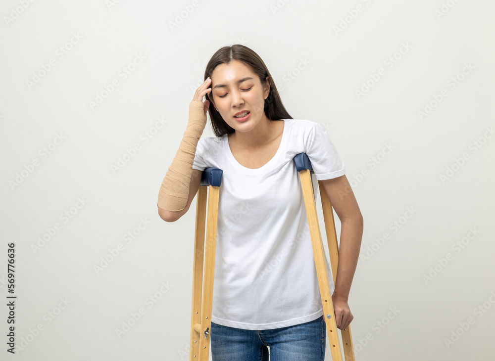 Happy young asian woman broken arm and leg on isolated. Woman put on plaster cast splint with walking sticks crutches. Patient wearing sling support arm with neck collar. life insurance and accident