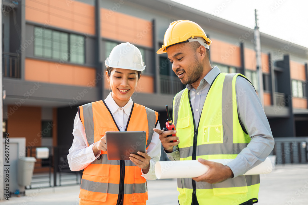 Two Asian worker engineer architect man and woman architect looking construction with white safety helmet in modern home building construction. Work planning with blueprint and tablet. Two Asian worker engineer architect man and woman architect looking construction with white safety helmet in modern home building construction. Work planning with blueprint and tablet.
