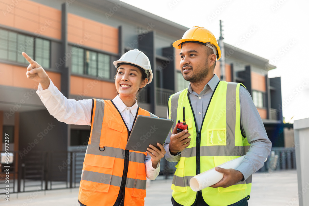 Two Asian worker engineer architect man and woman architect looking construction with white safety helmet in modern home building construction. Work planning with blueprint and tablet. Two Asian worker engineer architect man and woman architect looking construction with white safety helmet in modern home building construction. Work planning with blueprint and tablet.
