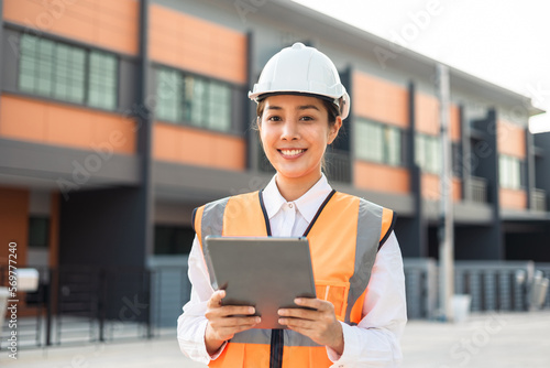 Confident asian engineer woman Using tablet for checking and maintenance to inspection at modern home building construction. Architect working with white safety helmet in construction site