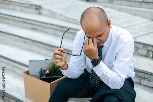 Sadness depressed Businessman with box cardboard packing personal items after losing jobs. Failure businessman sitting at stair front of building. Your fired Unemployed Jobless People Crisis photo