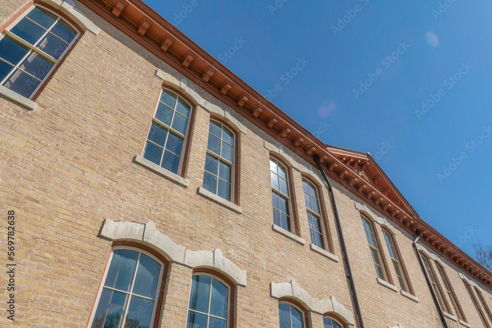 Low angle view of a building with bricks and paned windows in Austin, Texas. Building exterior with brown roof dentils against the clear blue skies. Low angle view of a building with bricks and paned windows in Austin, Texas. Building exterior with brown roof dentils against the clear blue skies.