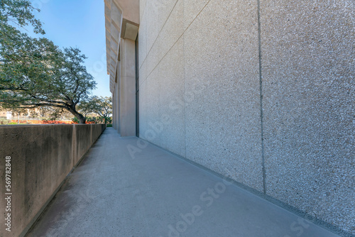 Walkway outside the building with concrete barrier near the small stones wall- Austin, Texas. Balcony hallway with views of trees and clear blue skies.