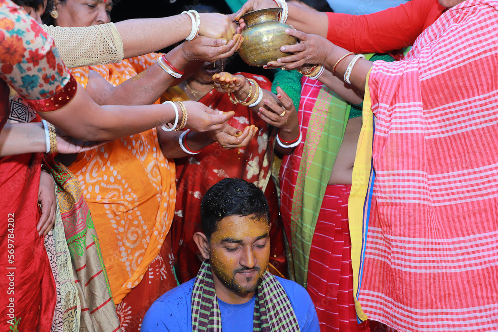 Hindu religious asian groom having bath by her aunts in his pre wedding ceremony, turmeric on
