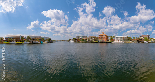 Panorama of water and villas with yachts at front in Destin Harbor- Destin, Florida. There are buildings on the shore with boats at the front.