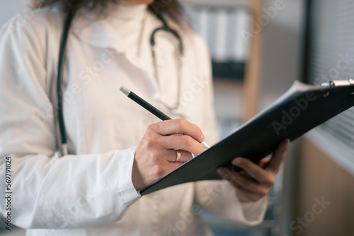 Close up of female doctor hands with clipboard. Taking notes to clipboard while standing in hospital. Health care medical background. Medical Services.
