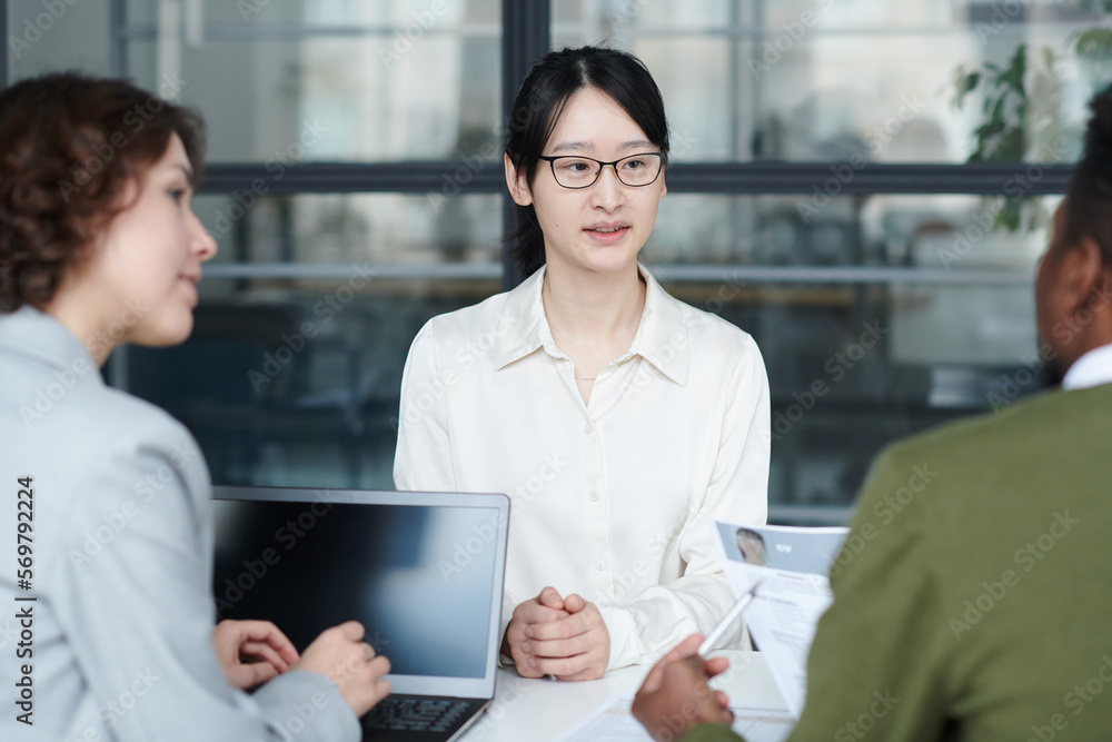Asian young candidate sitting at table and discussing her resume together with managers at job interview Asian young candidate sitting at table and discussing her resume together with managers at job interview