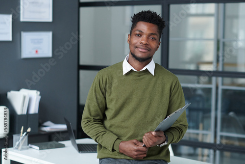 Portrait of African American businessman looking at camera standing in modern office with his workplace in background