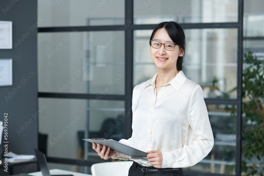 Portrait of Asian young businesswoman smiling at camera while working with documents in modern office Portrait of Asian young businesswoman smiling at camera while working with documents in modern office
