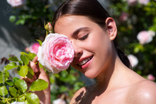Beautiful natural woman in the garden of roses. Sexy woman enjoying flowers over spring garden background. Rose spring garden.