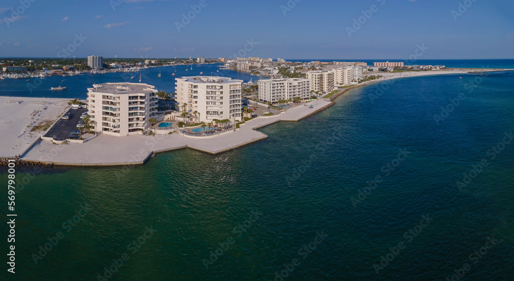 Coastline hotels condominiums in the middle of blue ocean water at East Jetty in Desti, Florida. Aerial shot view of waterfront modern multi-storey buildings with boats at the waterway behind.