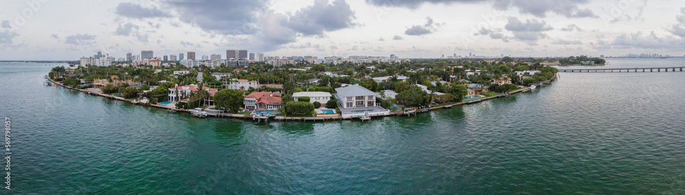 Panorama of Miami Beach Florida with buildings surrounded by calm water. Aerial coastal landscape of waterfront houses against cloudy blue sky.