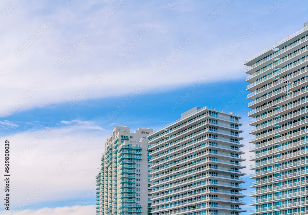 Row of modern apartments in Miami, Florida under the giant flat clouds in the sky. Three high-rise apartments with glass balcony railings.