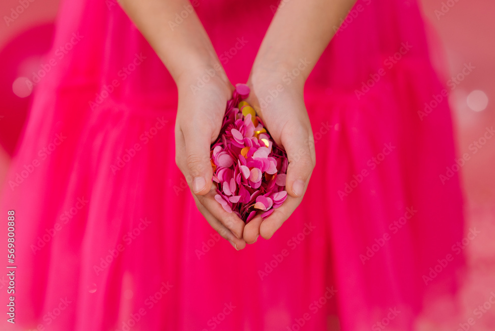 Bright pink and gold paper confetti in the palms of a birthday girl in a dress at a party Bright pink and gold paper confetti in the palms of a birthday girl in a dress at a party