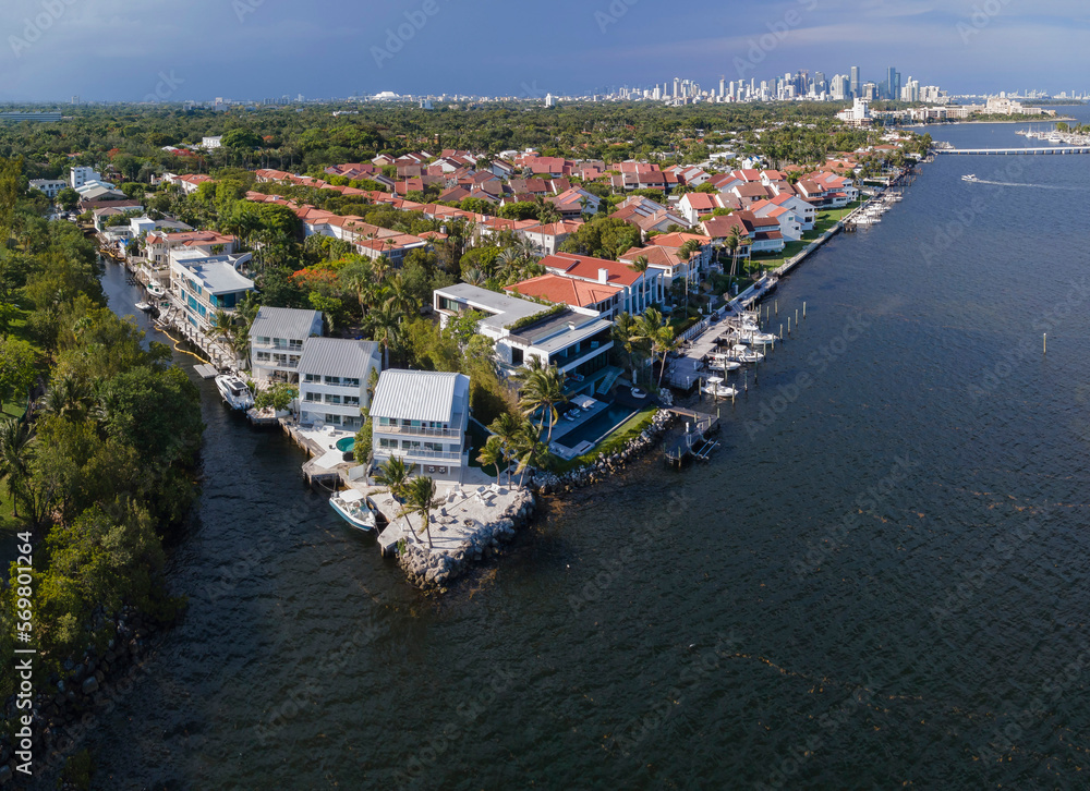 Aerial view of waterfront residences near the forest isolated from the city at Miami, Florida. Wealthy neighborhood with single-family homes near waterway on the left and views of high-rise buildings.