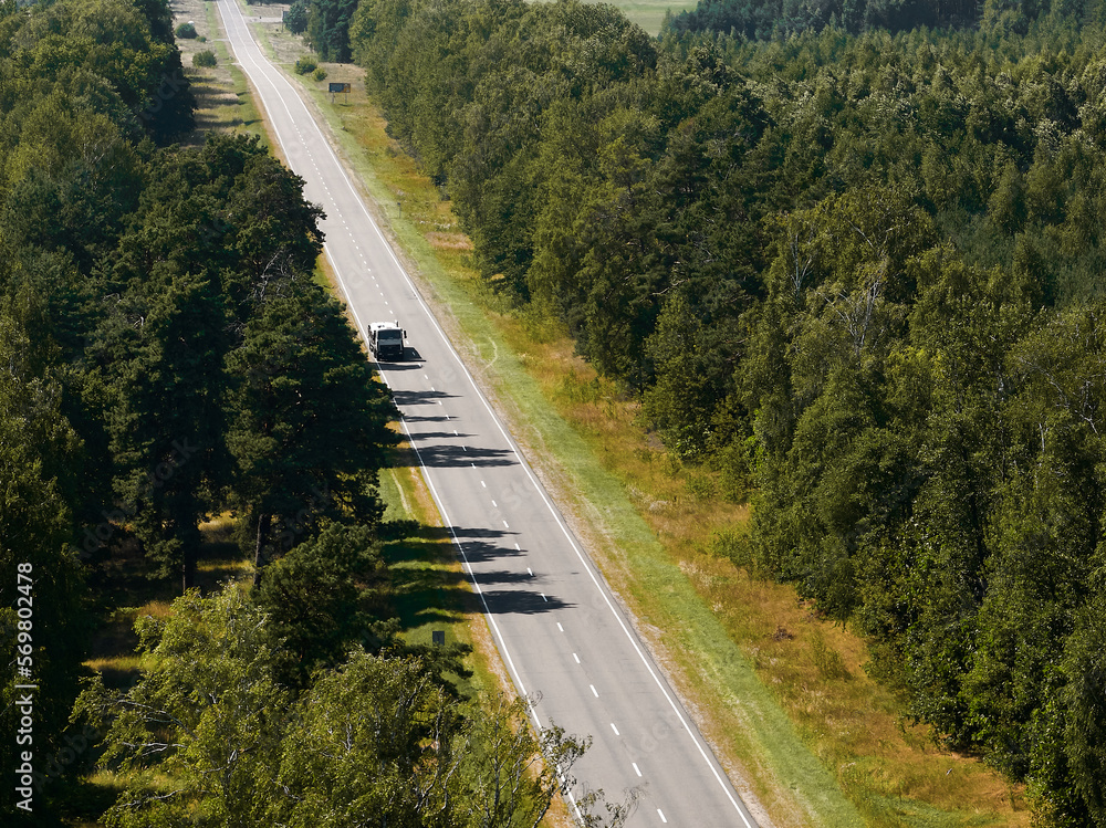 Moving cars on highway between green forests among fields