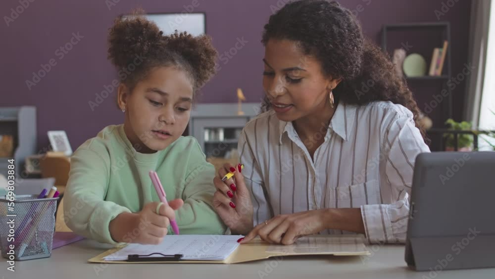 Young Biracial woman and her pretty little daughter doing homework together in bright modern living room Young Biracial woman and her pretty little daughter doing homework together in bright modern living room
