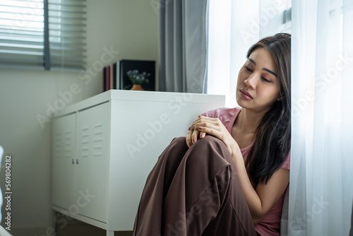 Asian young upset depressed woman sitting alone in living room at home.