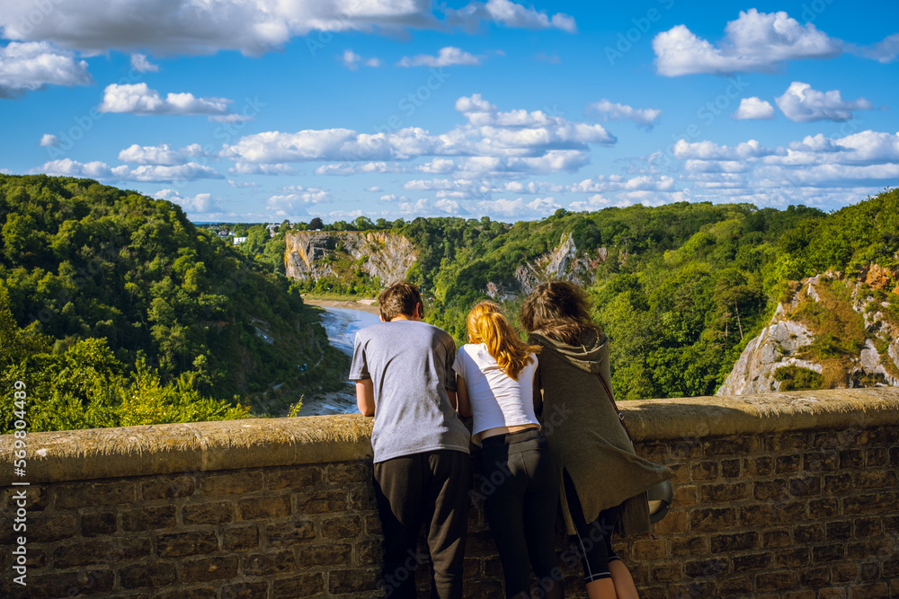 Mature mother with teenage son and daughter standing on tall bridge enjoying the view below; blue sky with clouds in background Mature mother with teenage son and daughter standing on tall bridge enjoying the view below; blue sky with clouds in background