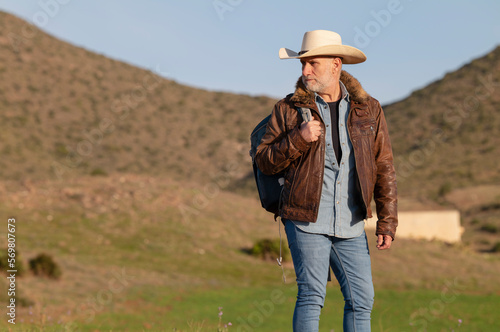 Adult man on cowboy hat standing on hill against mountain © WeeKwong