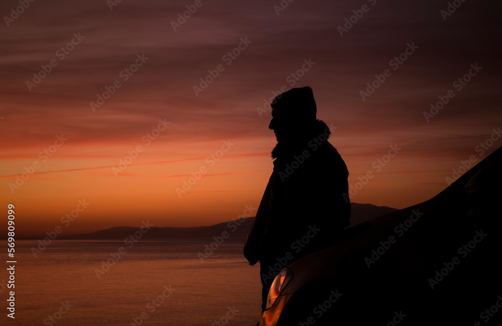 Silhouette of man with his car against sea and sky during sunset