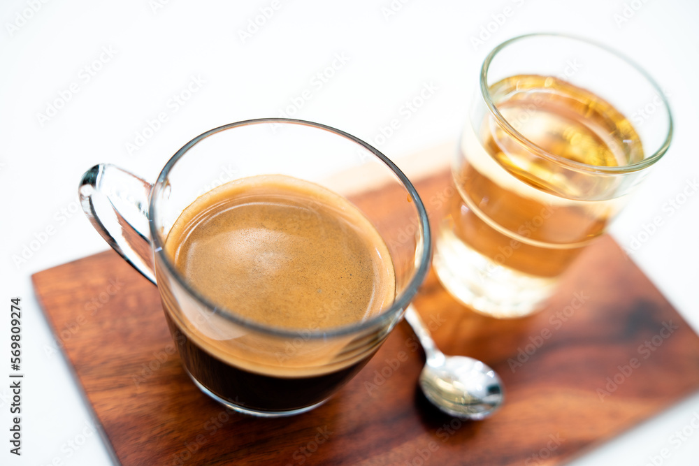 Crema of black coffee in a clear glass on a wooden tray, with a clear tea glass next to it selective focus, soft focus. Crema of black coffee in a clear glass on a wooden tray, with a clear tea glass next to it selective focus, soft focus.
