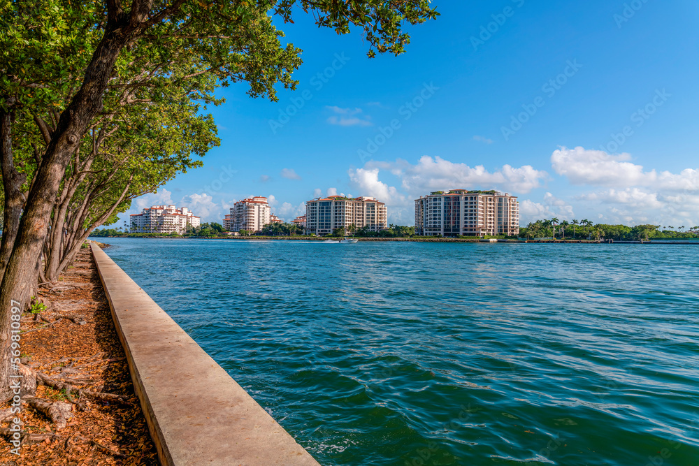 Palazzo Della Luna, Fisher Island seen from South Point Park in Miami, Florida. There are trees on the right side near the concrete seawall and a view of modern residential buildings across the water.