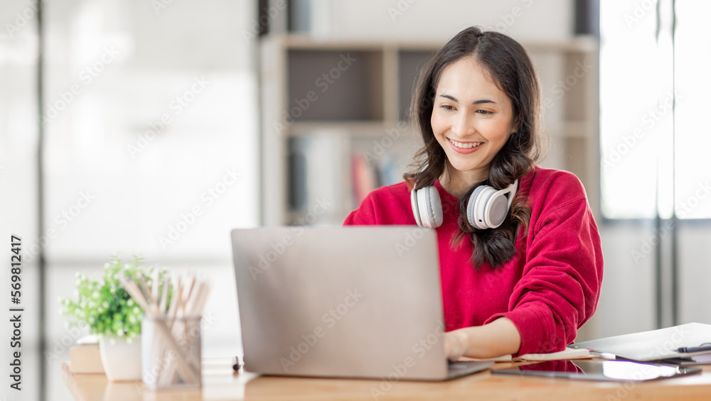 Portrait of Young asian woman wearing headphones using laptop in cafe, writing notes, learning language, watching online business or education concept Portrait of Young asian woman wearing headphones using laptop in cafe, writing notes, learning language, watching online business or education concept