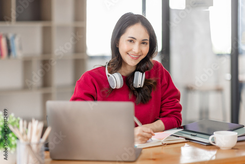 Portrait of Young asian woman wearing headphones using laptop in cafe, writing notes, learning language, watching online business or education concept © David