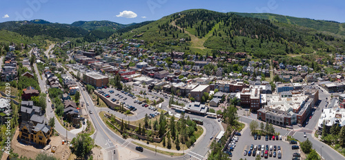 Fototapeta Naklejka Na Ścianę i Meble -  Scenic residential community in the mountains of Park City Utah on a sunny day. Aerial view of houses, buildings, roads, and cars against trees and green field with blue sky.