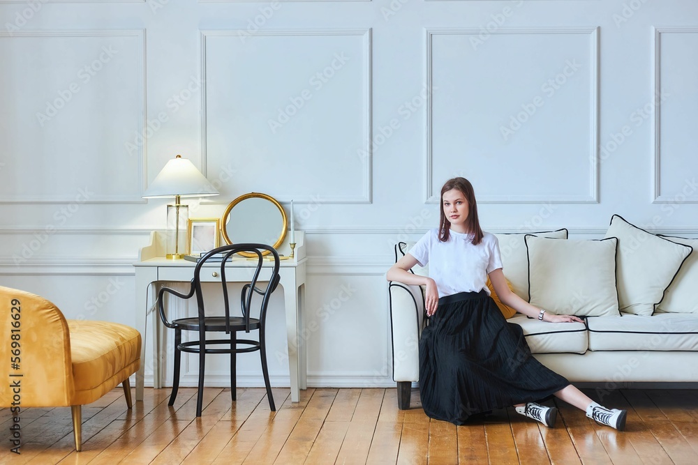 A young beautiful girl is sitting on a sofa in a stylish vintage room A young beautiful girl is sitting on a sofa in a stylish vintage room