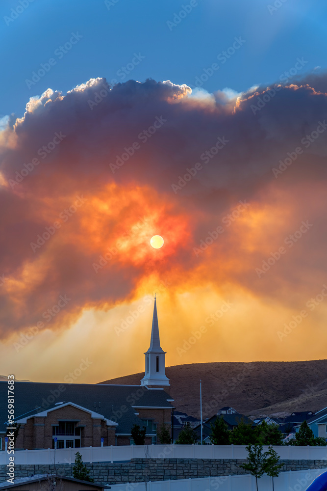 July 9, 2022, Utah- Views from Eagle Mountain of a smoke from Jacob Fire during sunset. Giant clouds covering the sunset with silhouttes of smoke and mountains behind LDS church below.