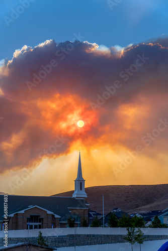 July 9, 2022, Utah- Views from Eagle Mountain of a smoke from Jacob Fire during sunset. Giant clouds covering the sunset with silhouttes of smoke and mountains behind LDS church below. © Jason